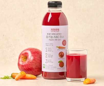 Bottle of whole-ground Organic ABC juice for E-Mart's Jeju brand, beside an apple, a carrot and a filled glass