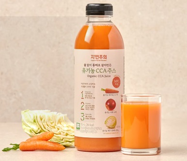 Bottle of whole-ground Organic CCA juice for E-Mart's Jeju brand, beside cabbage, a carrot and a filled glass