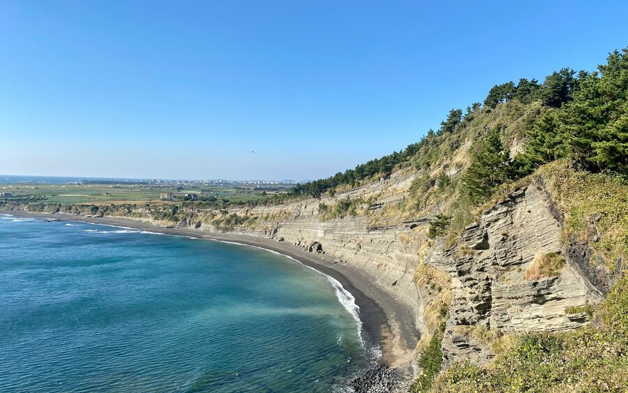 Layered volcanic cliff strata on the Jeju coast, the island's UNESCO Global Geopark.